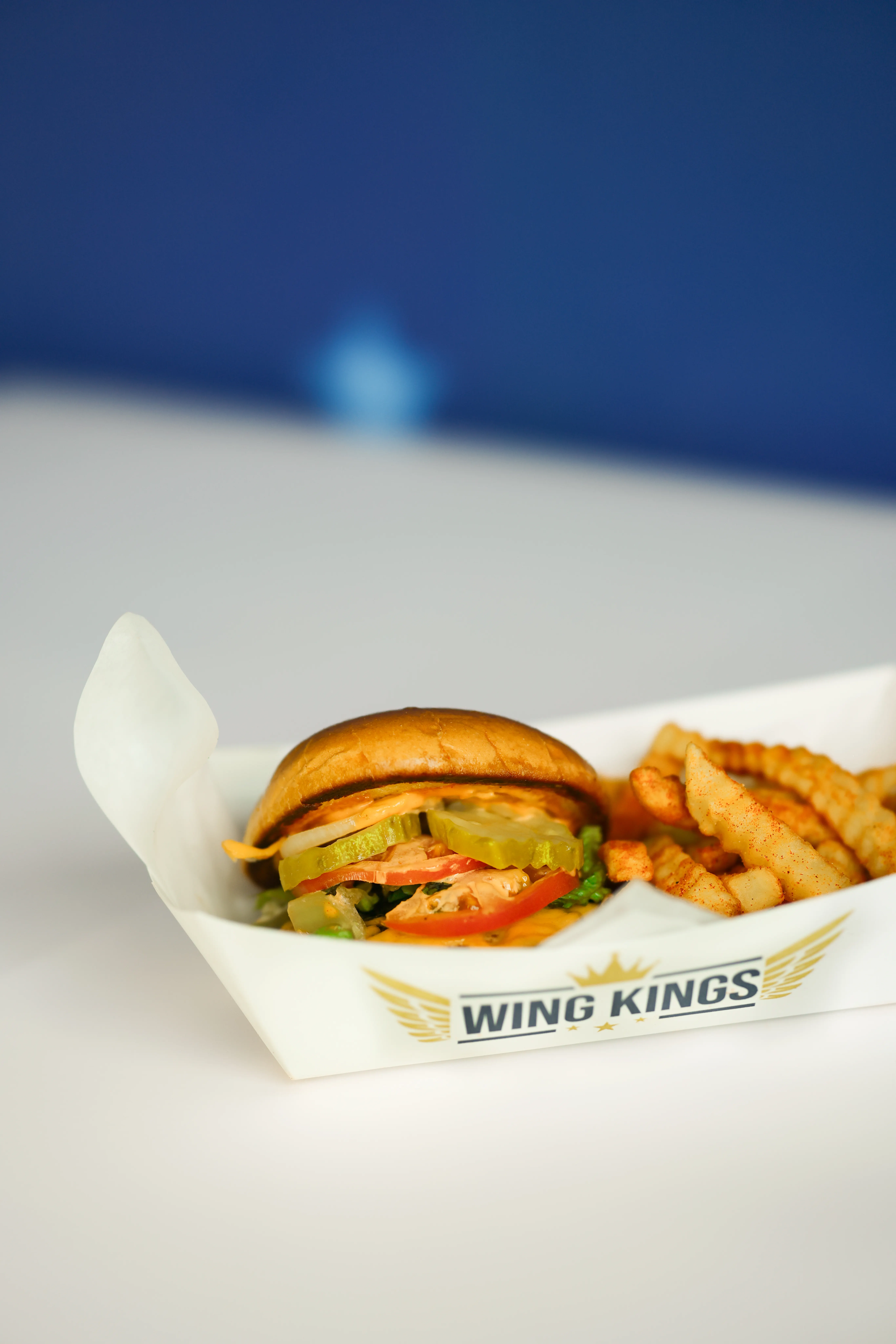 The WK burger and crinkle fries in a paper boat, against the painted blue wall of the store