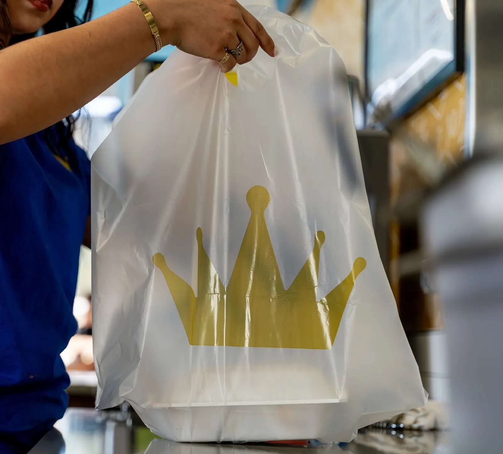 A Wing Kings employee handing a white takeout bag with the gold crown across the front counter