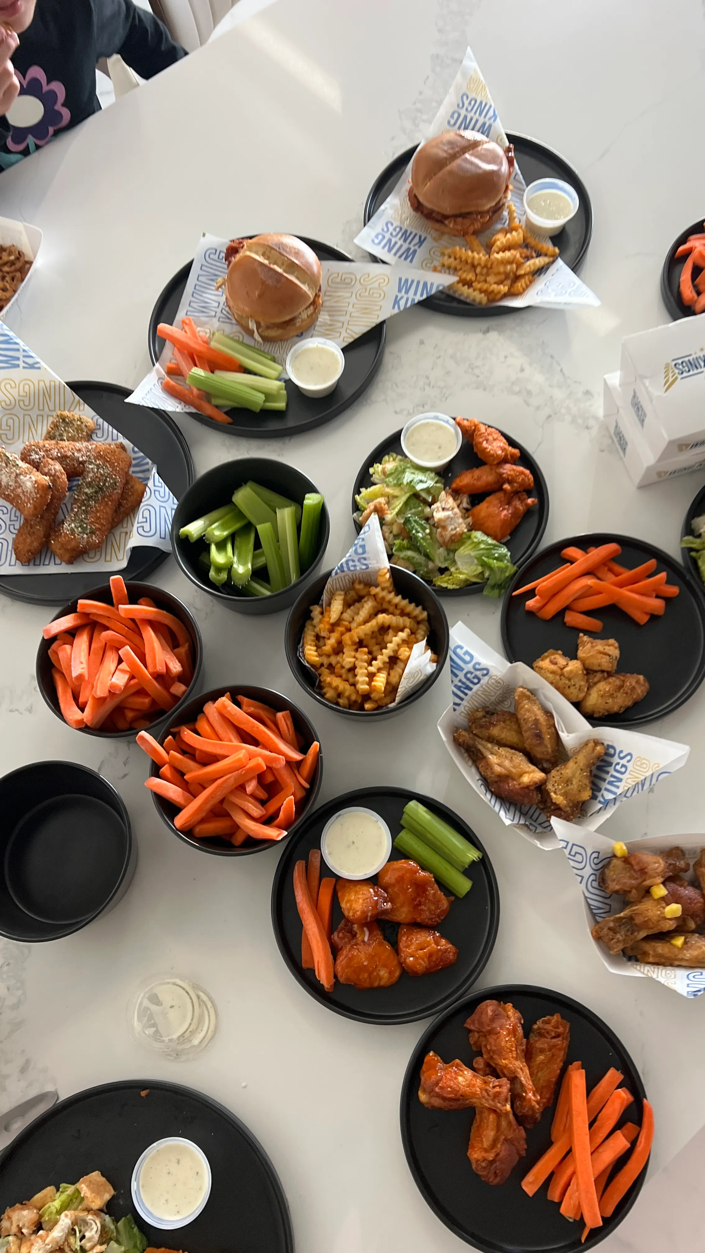 An overhead spread of Wing Kings trays across a table: sauced wings, crinkle fries, carrots and celery with ranch cups