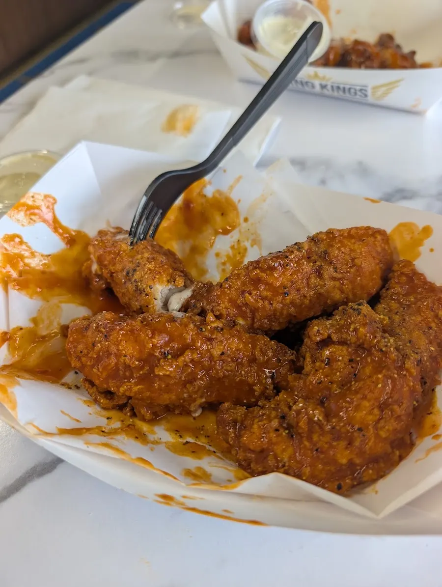 Customer photo: sauced chicken tenders in a paper boat, a Wing Kings boat behind them, at Wing Kings Trawood