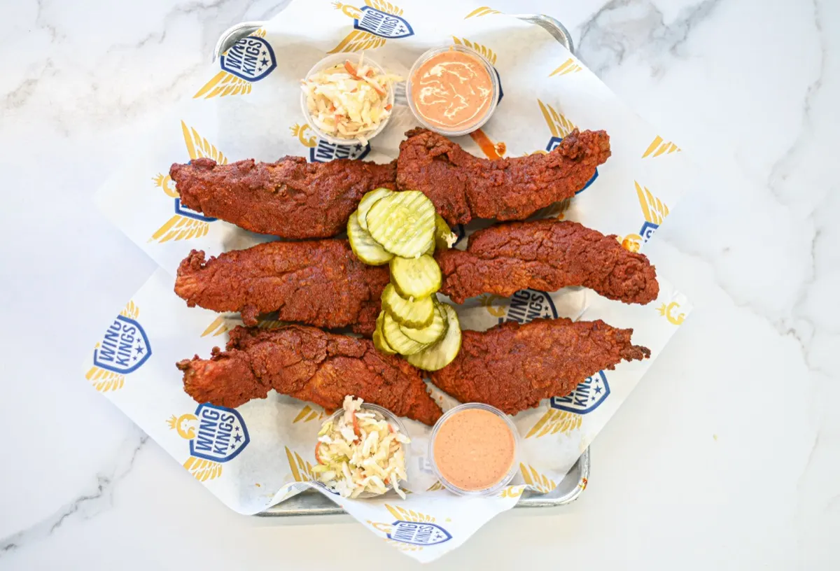 Nashville tenders on branded paper in a steel tray with pickle chips, slaw and a dip cup, on white marble